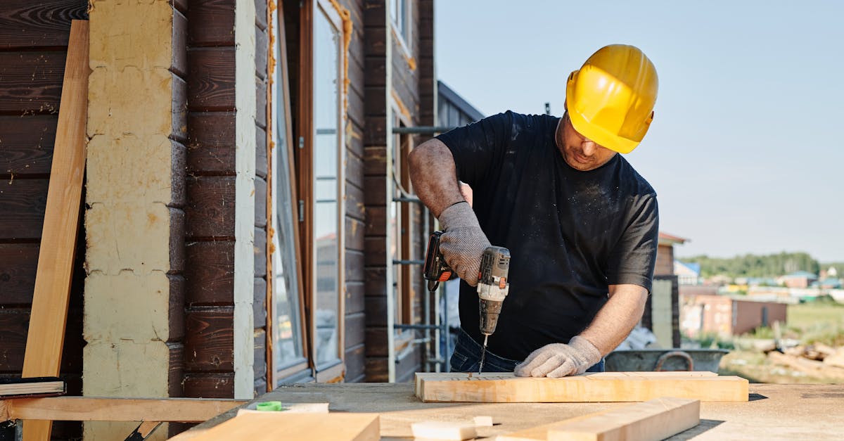 A construction worker using a power drill on a building site, outdoors during the day.
