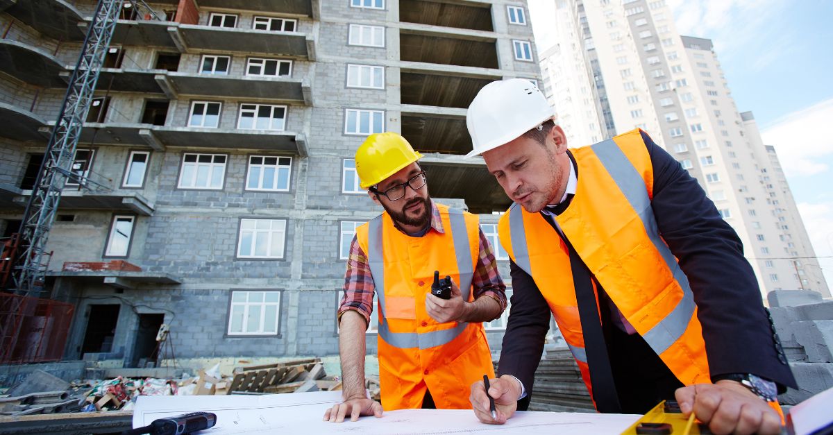 construction workers looking at plans outside a housing estate with flats in background uk